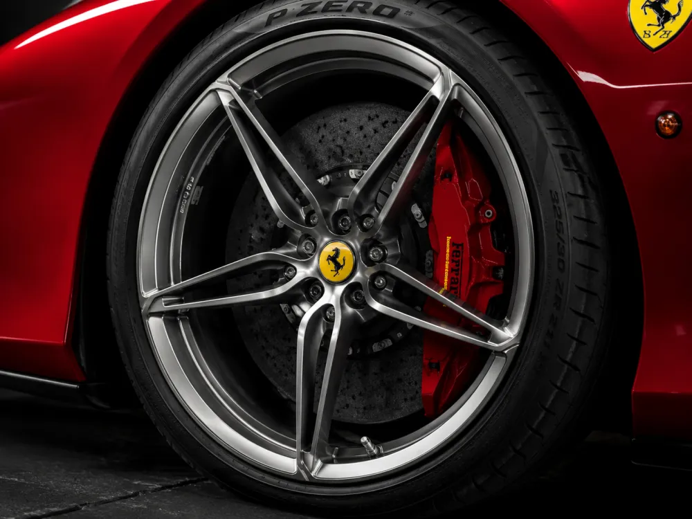 A close-up studio image of high end rims on a Ferrari, showing polished spokes, performance brake calipers, and premium ti