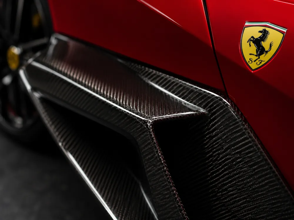 Close-up of a Ferrari carbon fiber exterior component with visible weave texture, dramatic studio lighting,
