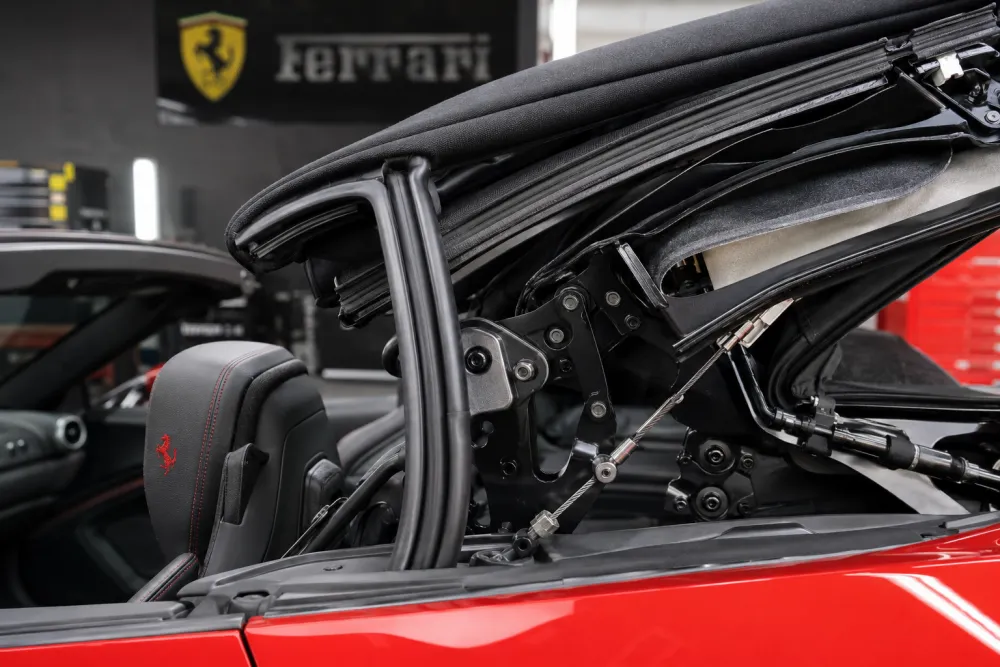 Detailed macro shot of a Ferrari convertible roof mechanism with frame joints, seals, tension cables, and fabric layers visible, premium automotive service bay lighting