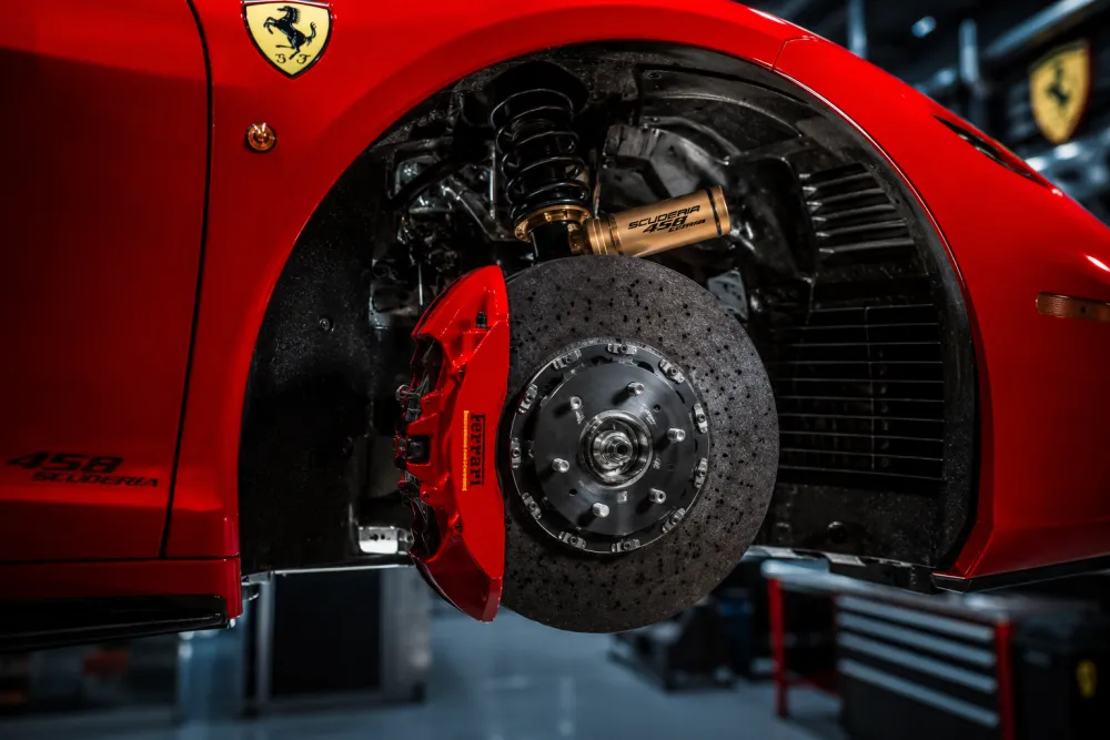 Ferrari 458 Scuderia inspired wheel, brake, and suspension detail showing performance-focused luxury-car parts in dramatic workshop lighting