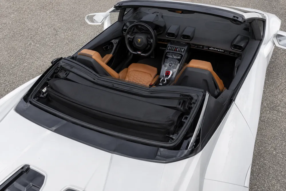 Lamborghini convertible interior viewed from above with the roof open, showing elegant leather seats, weather seals, rear deck, and folded soft roof storage area 